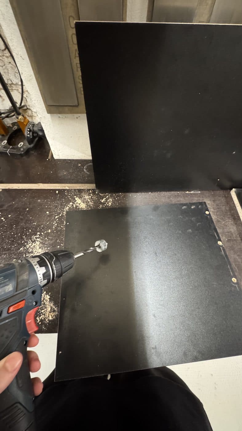 Drilling dowel holes into a black panel at a rented workbench.